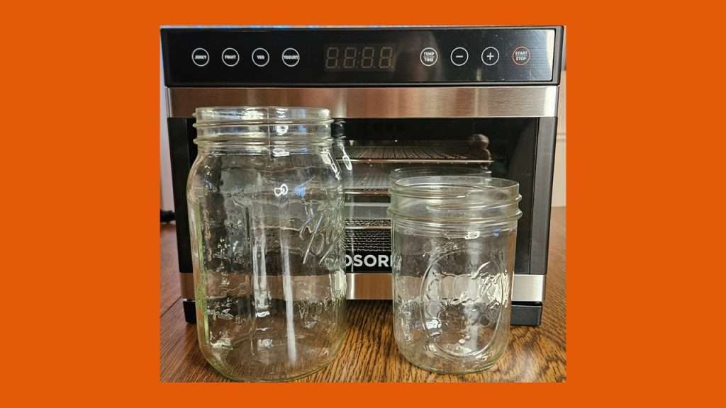 The Cosori 5 tray mini dehydrator with mason jars in front of it to help show the size.