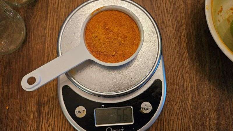 Measuring cup filled with pumpkin powder placed on a digital scale reading 56 grams.