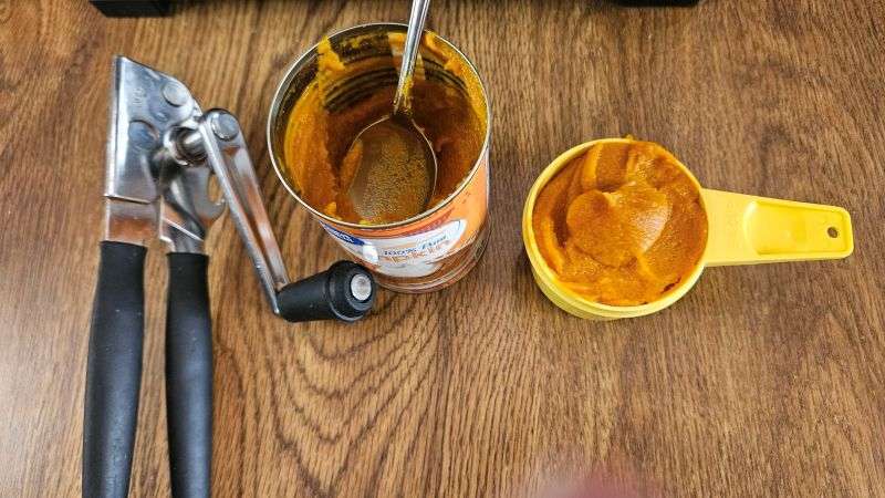An open can of pumpkin next to a measuring cup holding pumpkin puree.