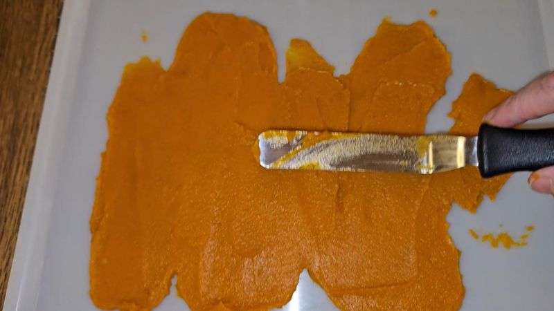 Pumpkin puree being spread on a dehydrator tray using an offset spatula.