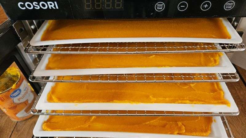 Multiple dehydrator trays with pumpkin puree partially pulled out of a Cosori dehydrator.