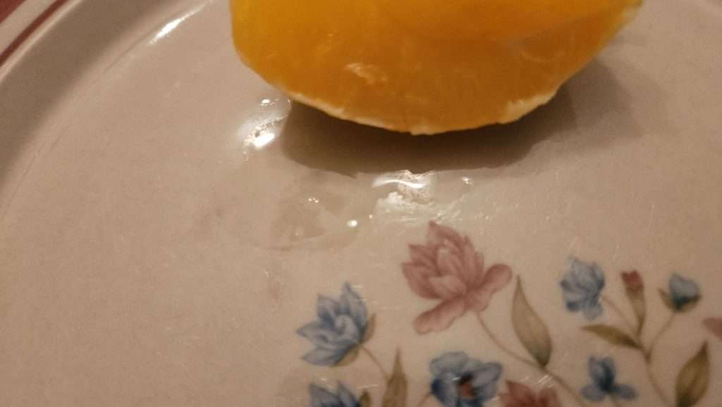 Thawed orange quarter on a plate with a small amount of juice after thawing