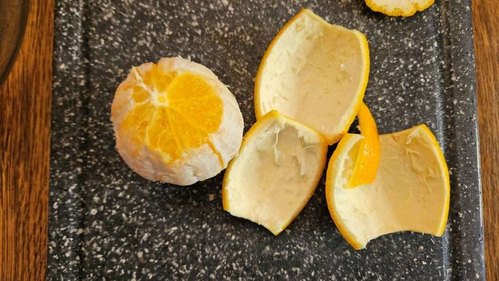 Peeled orange next to removed peel sections while preparing oranges for freezing