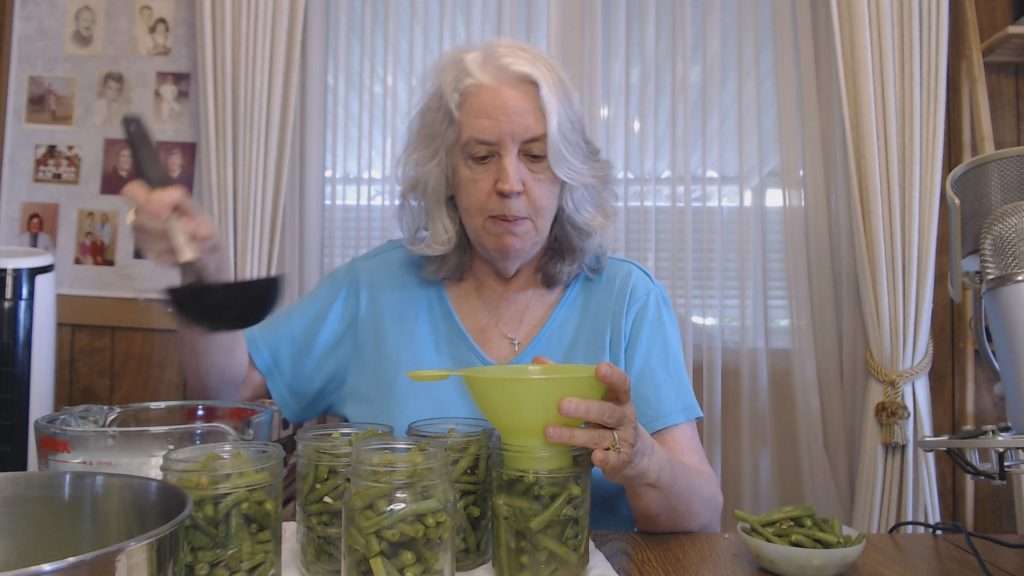 Using a canning funnel to add water to canning jars filled with lemon garlic green beans.