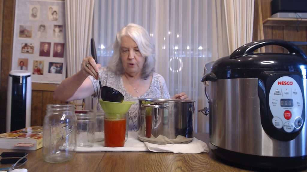 Using a ladle to pour strawberry lemonade concentrate into a mason jar.