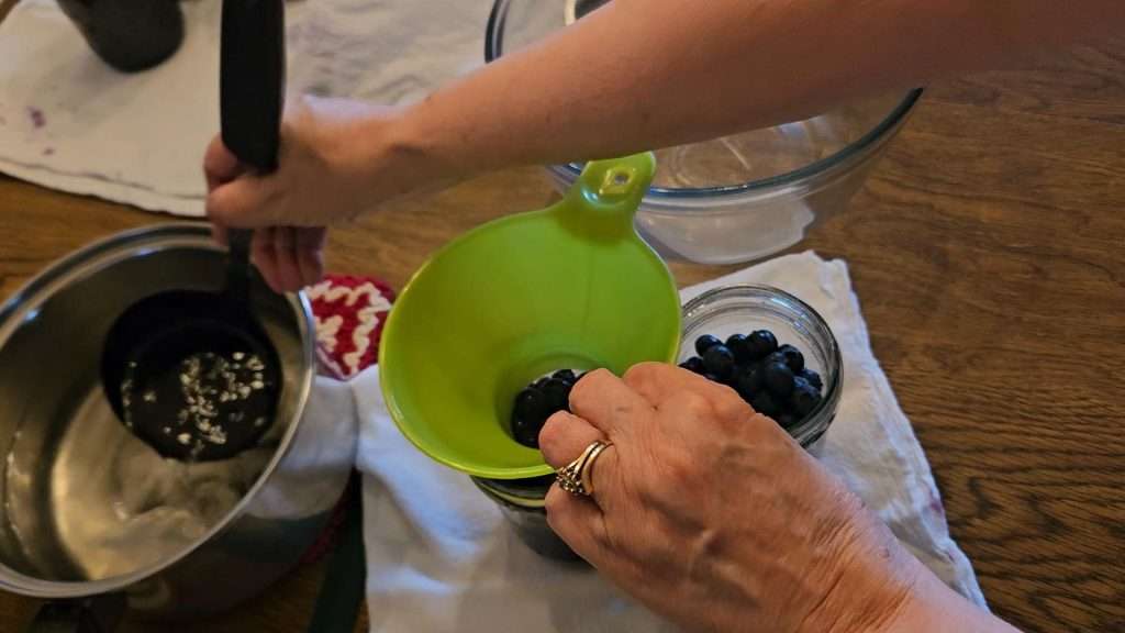 adding hot syrup to raw pack blueberries for canning.