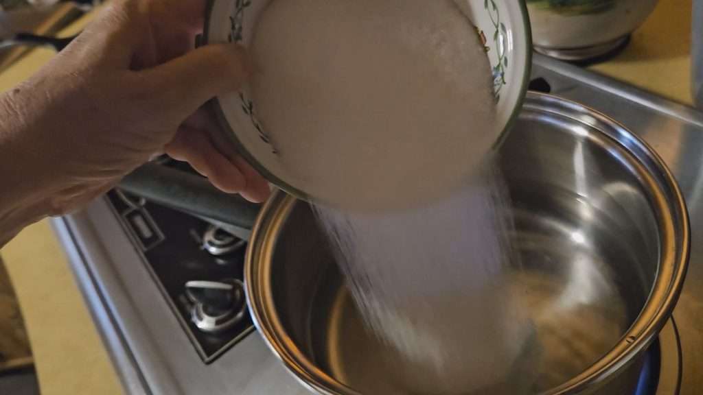 Pouring sugar into a bowl to make a light simple syrup for canning grapes.