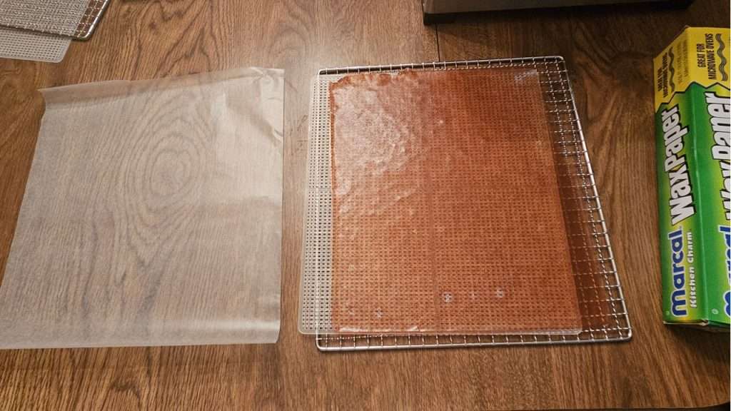 a dehydrator tray with grape fruit leather to the right of a piece of wax paper.