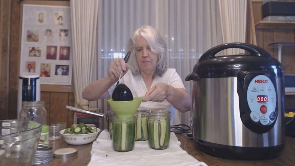 Adding pickle brine to the jars filled with cucumber spears.