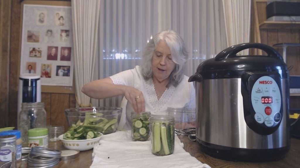 Adding cucumbers to canning jar.