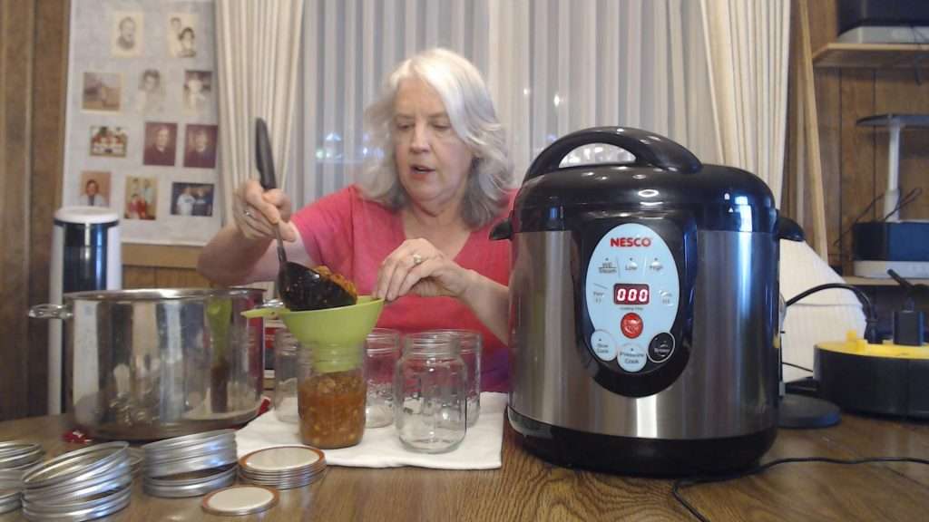 Filling wide-mouth canning jars with hot chili con carne.