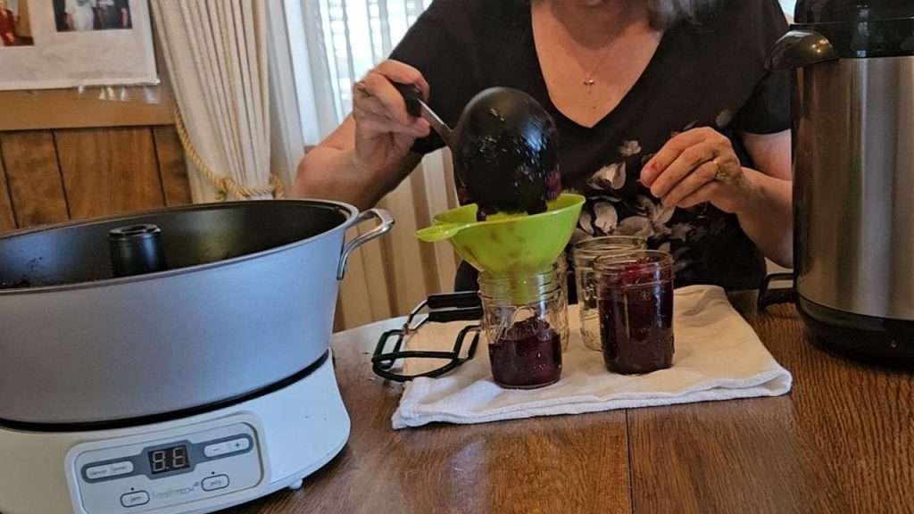 Using a ladle to put hot cranberry sauce into canning jars.