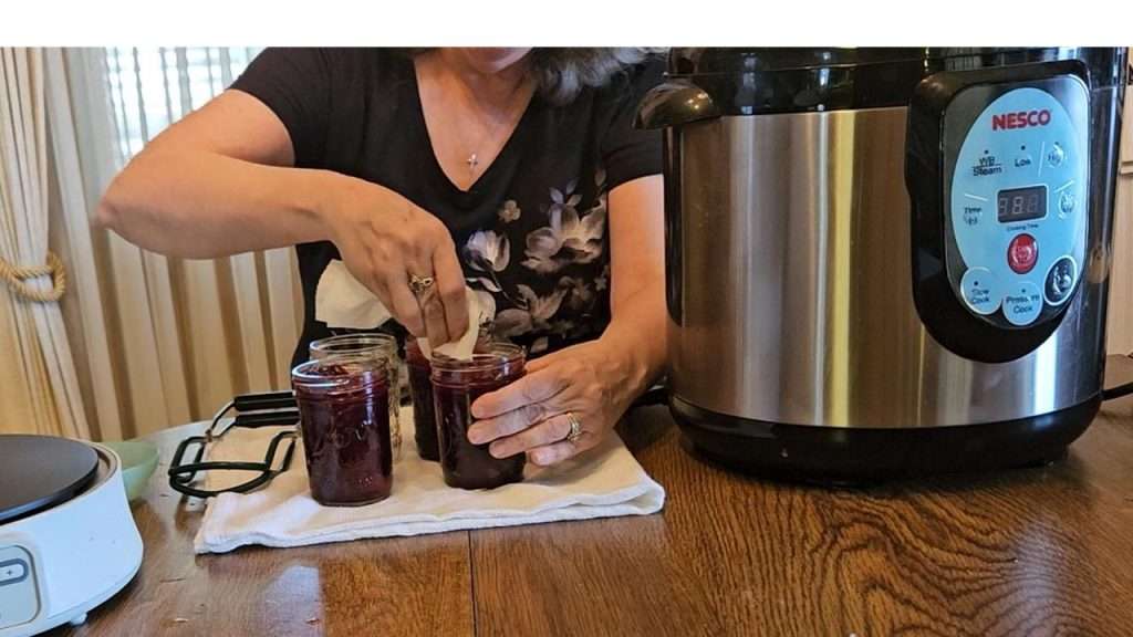 Wiping the rims of canning jars filled with cranberry sauce.