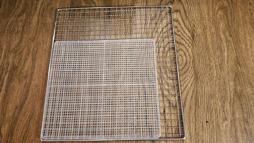 The stainless steel dehydrator rack of the Cosori 6-tray premium stainless steel dehydrator, with the mesh sheet from the Cosori mini-dehydrator laid on top of it to compare the size difference between the two dehydrators.
