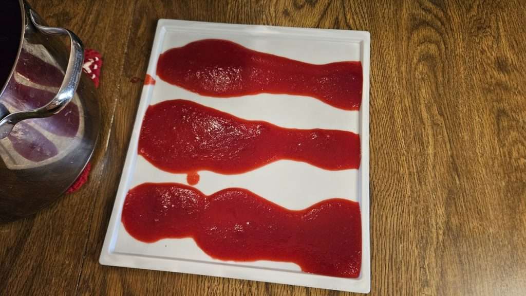 Pour cranberry puree onto fruit leather trays is a first step in evenly distributing the puree. Even distribution helps the cranberry fruit leather to dry evenly.