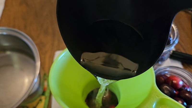 Ladle scooping syrup into jars full of cherries
