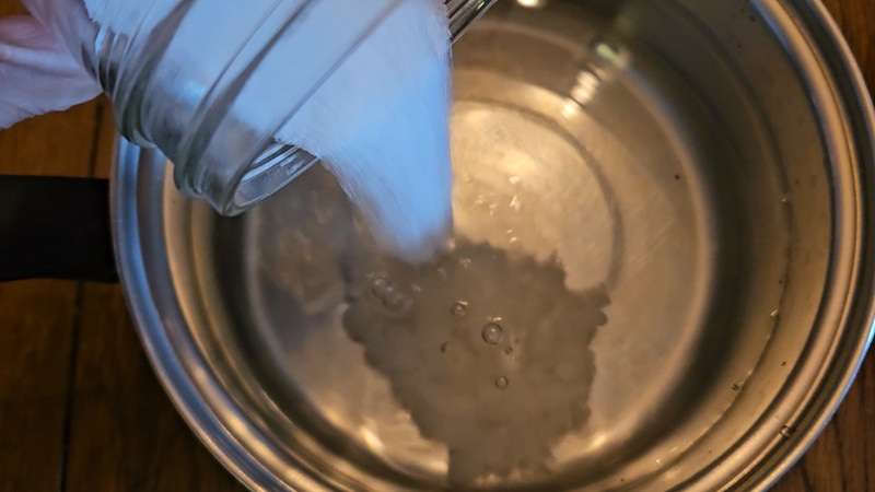 Sugar pouring from a glass mason jar into a stainless steel pot