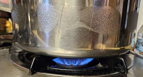 a stainless steel pot on a gas stove with the flame medium low