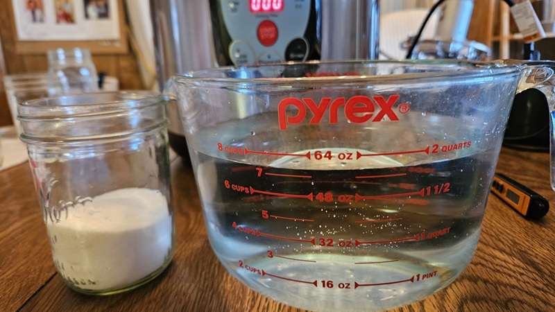 A Pyrex measuring cup with 7.5 cups of water next to a mason jar holding ¾ cup of sugar