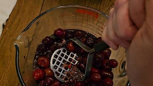 Mashing cherries for jam using a potato masher.