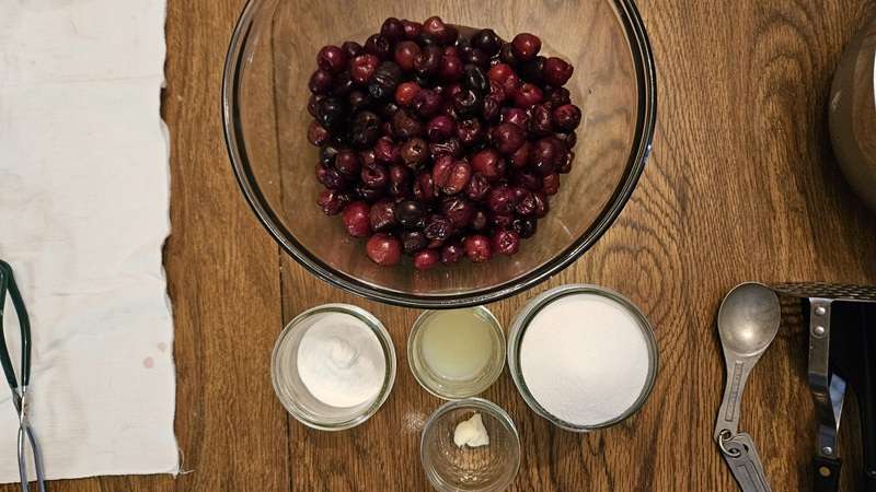 Ingredients for homemade cherry jam including cherries, pectin, lemon juice, sugar, and butter.
