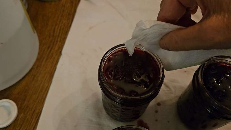 Wiping the rims on a jar of homemade cherry jam.