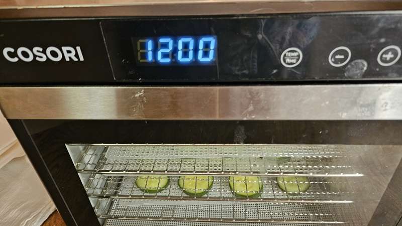A Cosori dehydrator filled with cucumbers with the time set for 12 hours.
