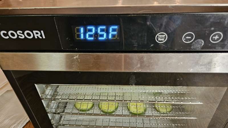 A Cosori dehydrator filled with cucumbers, with the temperature set at 125 degrees Fahrenheit.