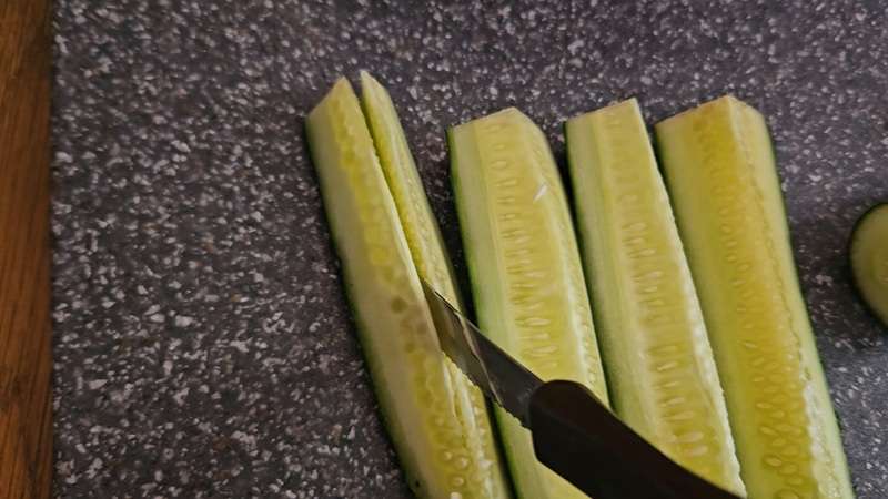 Using a knife to cut the cucumber 4ths in half, to end up with 8 spears per cucumber.