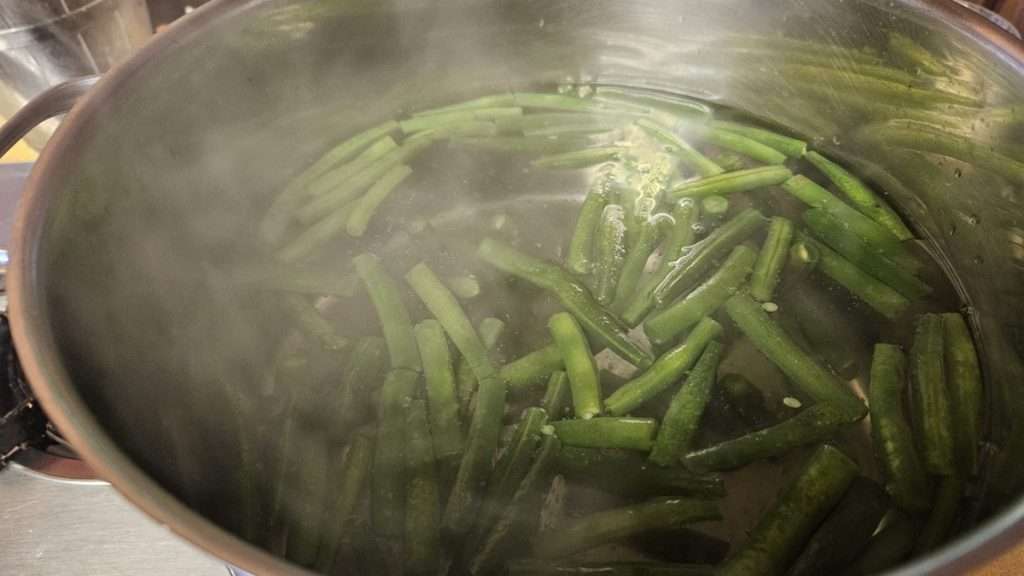 green beans in a pot of water. The water has stopped boiling due to the green beans being added in, but it is still hot.