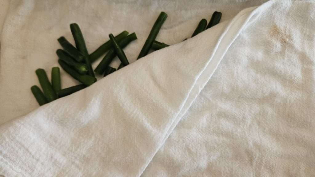 Green beans being patted dry with a flour sack towel