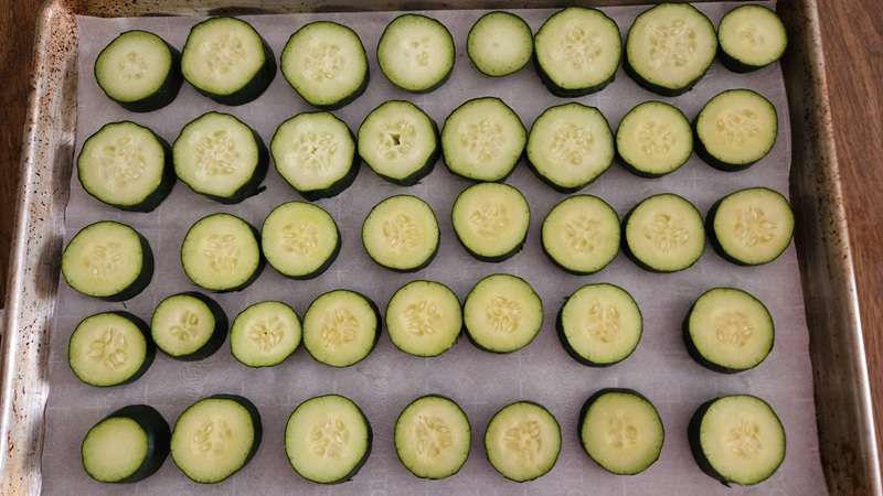 Cucumber rounds spaced apart on a tray lined with parchment paper, all ready to go into the freezer.