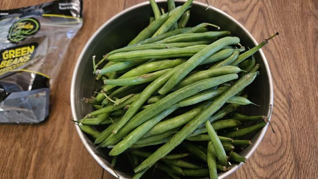 A bowl of green fresh green beans in a stainless steel bowl.
