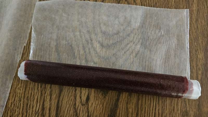 Cherry fruit leather being rolled up on a piece of wax paper.