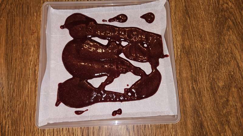 cherry fruit puree on strips on a parchment paper lined fruit leather tray.