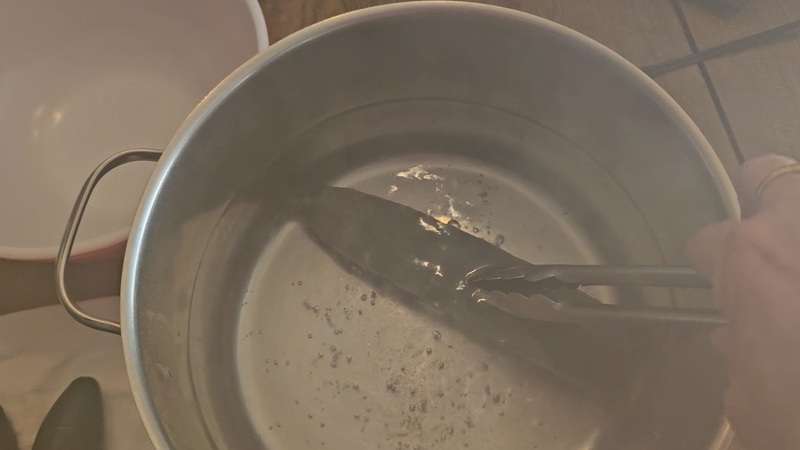 holding a cucumber down into boiling water with some tongs.