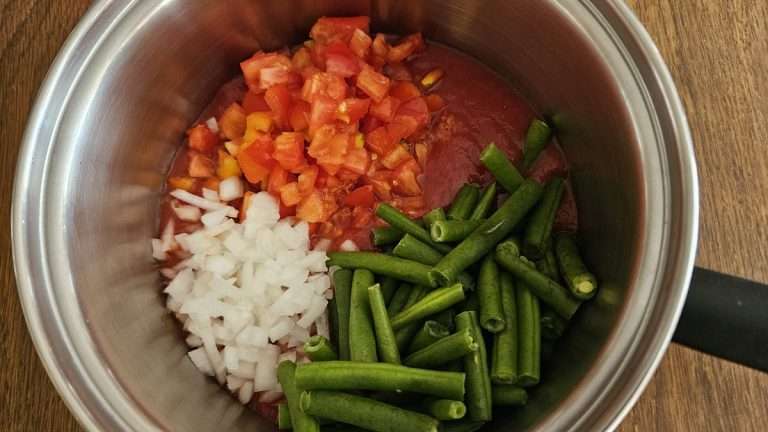 ingredients for freezing green beans and tomatoes in a stainless steel pot.