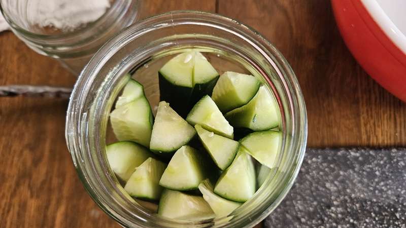 fresh cucumbers cut into spears and in a quart-sized mason jar, from a top view.