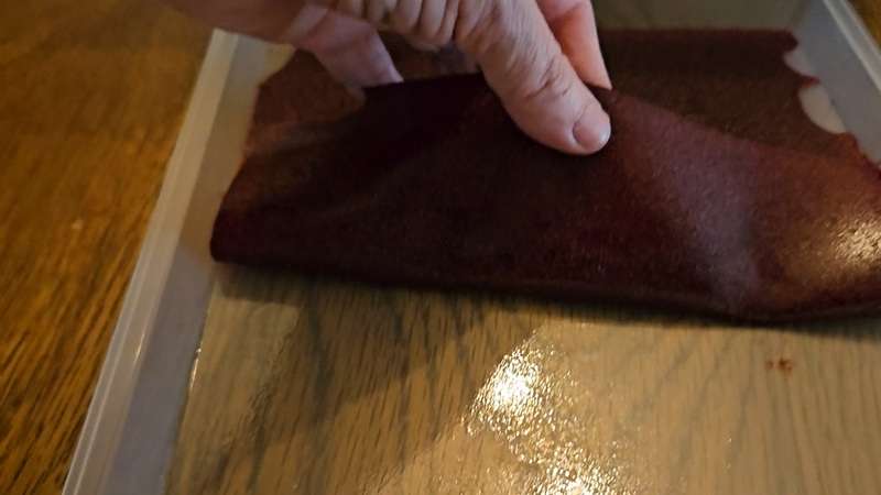Peeling cherry fruit leather from a fruit leather tray that has a little bit of oil on it.