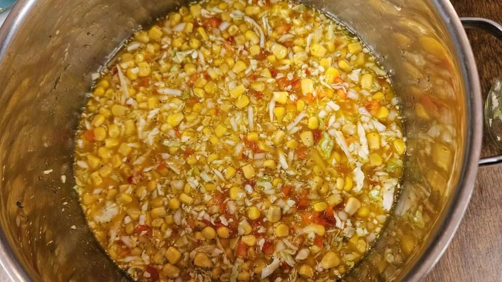 Corn relish ingredients all stirred together but uncooked in a stainless steel pot.