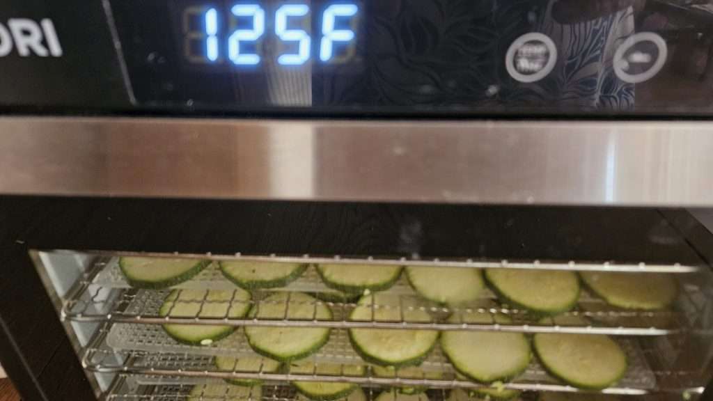 Cosori dehydrator with glass door showing zucchini slices inside, temperature set to 125°F.
