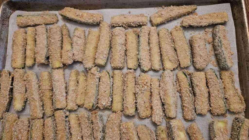 Breaded zucchini on a parchment paper lined baking sheet ready to go into the freezer.