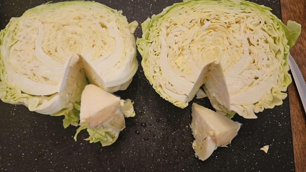 Two halves of cabbage, on a cutting board, with the core removed. The core from each half is sitting just below the cabbage halves.