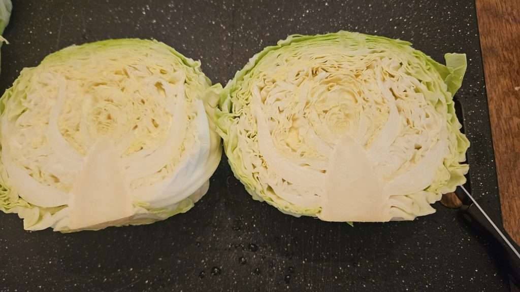 A head of cabbage cut in half, on a cutting board.