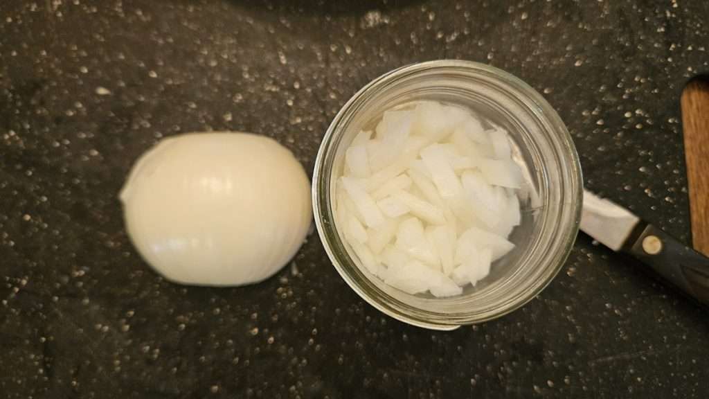 A half of an onion sitting next to a mason jar with diced onions.
