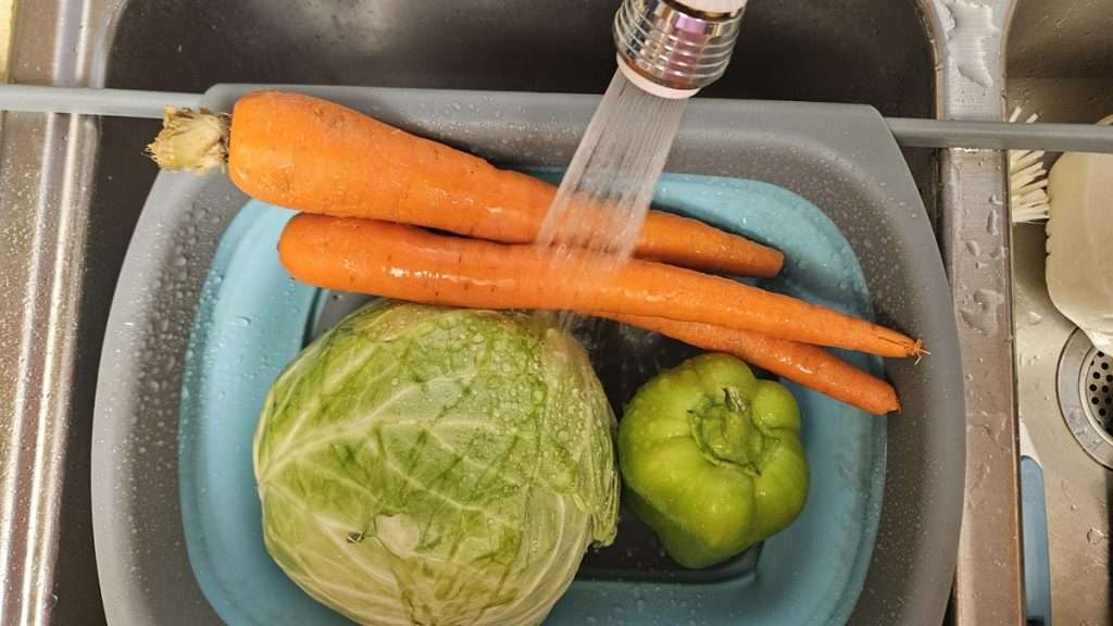 Cabbage, carrots, and bell pepper in colander being rinsed with water.