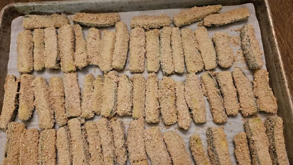 breaded zucchini on a parchment paper lined tray ready to go into the freezer.