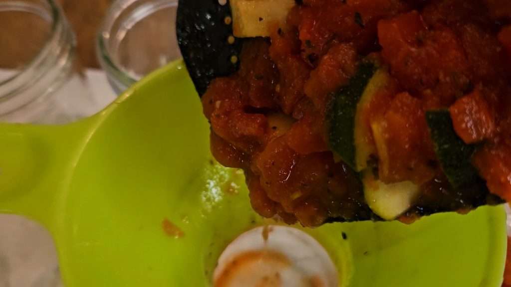 using a ladle to put zucchini and tomatoes into canning jar