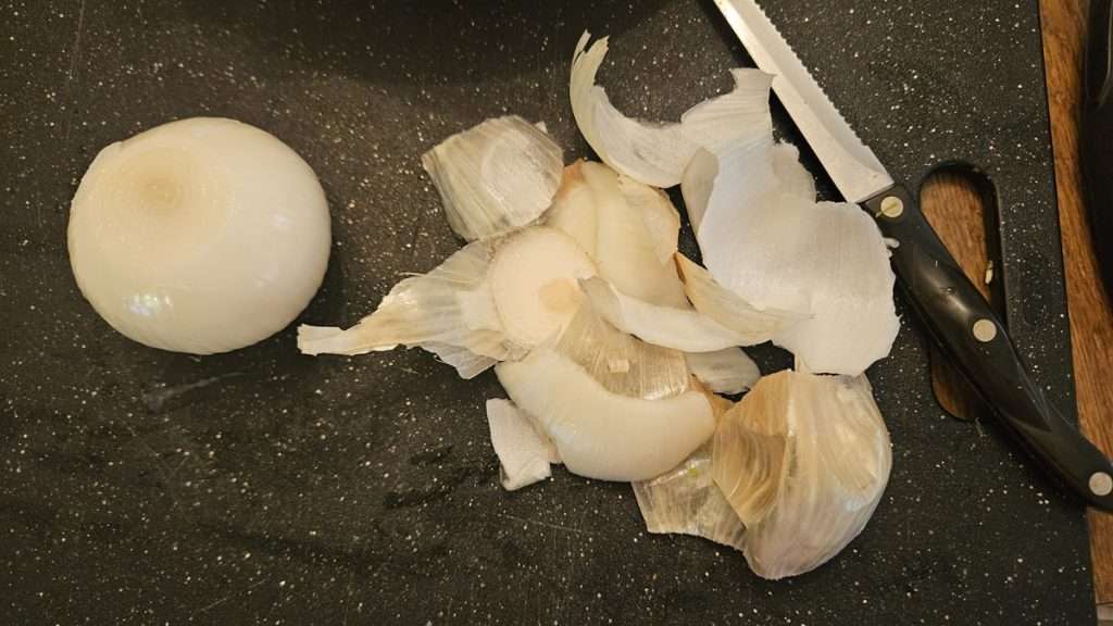 Peeled whole onion sitting next to a pile of onion peel.
