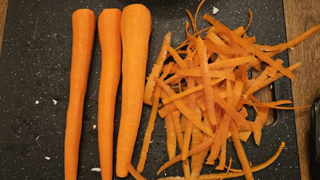 3 peeled carrots next to a pile of carrot peels.